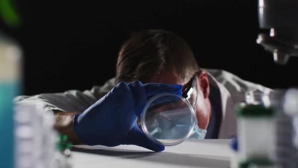 Caucasian male doctor wearing face mask and gloves inspecting petri dish