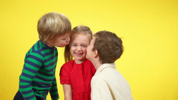 Two Boys Kissing Pretty Little Girl at Yellow Background