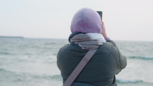 Woman Blogger in Warm Clothes Does Selphie on the Winter Beach