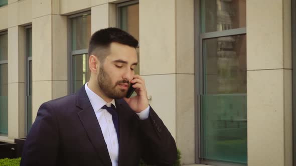 Young Businessman Feeling Annoyed While Talking on the Cell Phone Outdoors Near Office Building