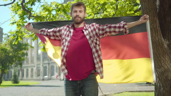 Portrait of Confident Positive Bearded Man Standing with Hands Spread on Sunny University Yard