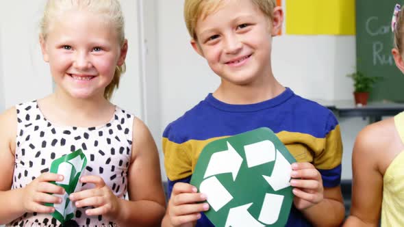 School kids holding recycling symbols and globe in classroom