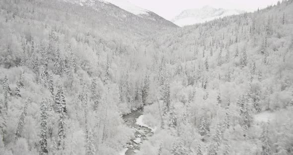 Aerial helicopter low flyover of Alaskan hillside, past train tracks, icy water, mountains, drone fo