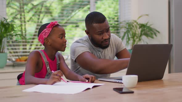 African american father using laptop and helping his daughter with homework at home
