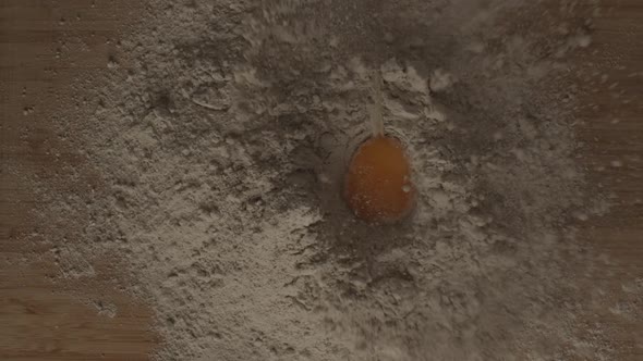 Studio product shot of egg falling in to flour on wooden table in slow motion.