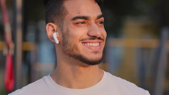 Smiling Middle Eastern Arab Millennial Man in Modern Headphones Posing Looking Aside at City Stadium