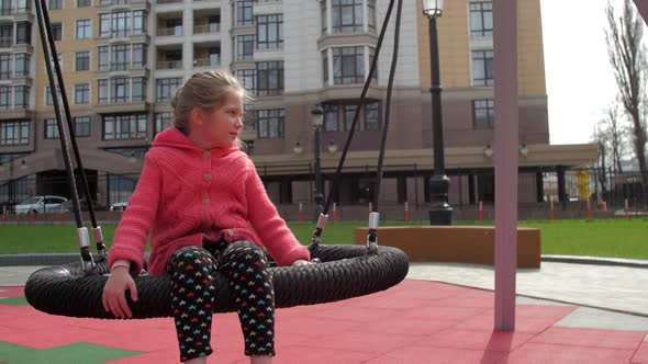 Calm Girl Kid Sits on Swing and Looks Around on Playground