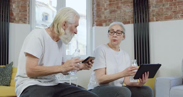 Old Couple Enjoying Joint Leisure and Watching Apps on Tablet Device and Phone