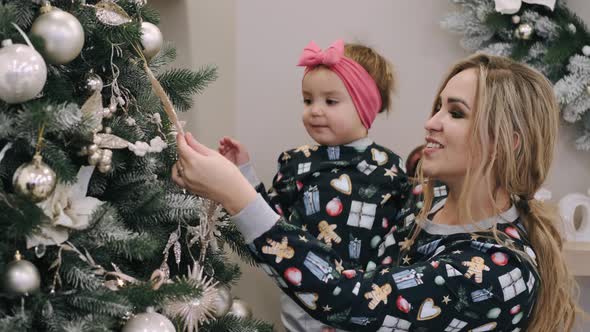 Festive Mother and Infant Daughter Decorating Christmas Tree at Home