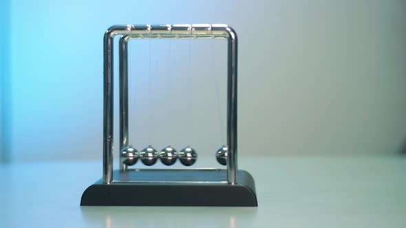 Newton's Cradle on the gray table with white and blue background. Metal balls on a thread in motion.