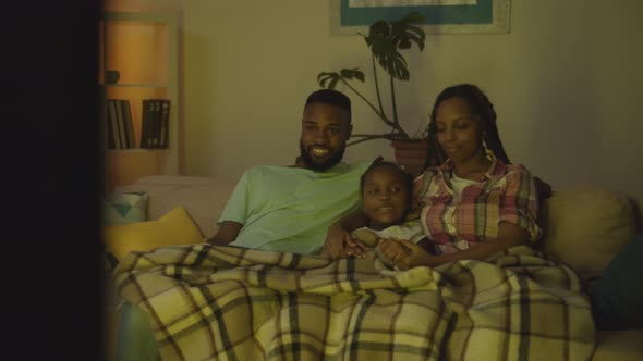 Happy African Family with Child Sitting on Sofa Watching Tv in Evening