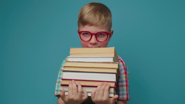 Schoolboy in Eyeglasses Holding Books and Smiling Looking at Camera Standing on Blue Background