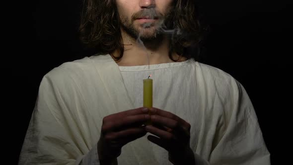 Male Sinner in Robe Emotionally Blowing Candle on Dark Background, Refusing God