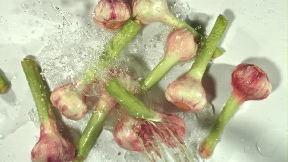 Super Slow Motion Garlic Falls Into the Ode with Splashes on a White Background