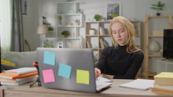 Young Blonde Woman Dreaming While Sitting at a Desk at Home While Studying