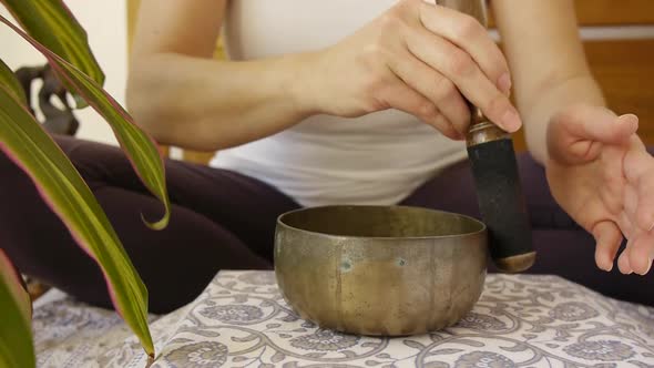 Sporty woman in yoga outfit playing Tibetan singing bowl as self care ritual.