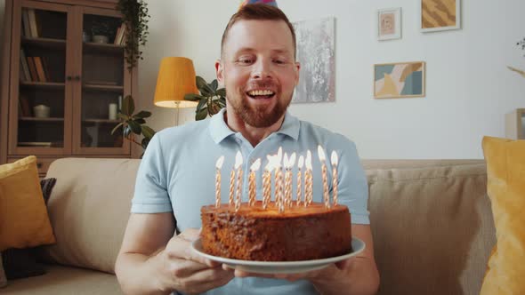 Happy Man Blowing Candles on Birthday Cake and Talking on Web Call