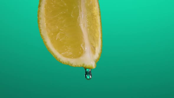 Super Slow Motion Macro Shot of Water Drop Falling From Lemon Slice on Blue Background