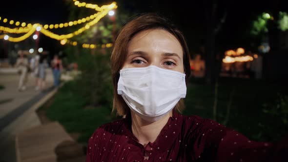 Young woman in medical face mask on a vacation takes a selfie on city background.Pov shot of woman.