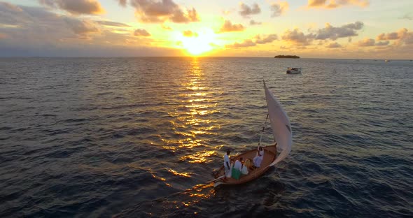 Aerial drone view of a man and woman sailing on a boat to a tropical island at sunset