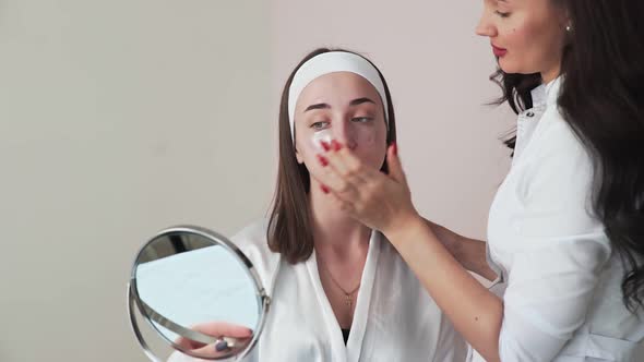 Young Woman with Collagen Pads Under Eyes Looks at the Mirror