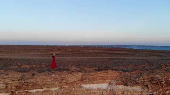 Aerial View of a Young Beautiful Woman in a Long Red Dress on a Mountain Rock Looking at the Sea a