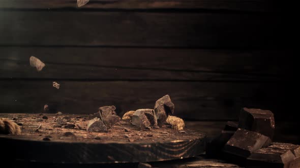 Super Slow Motion Falling Pieces of Dark Bitter Chocolate on a Wooden Board