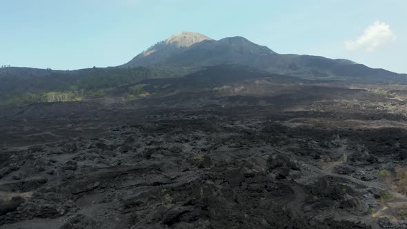 Aerial drone view flying over solidified black lava fields from an active volcano