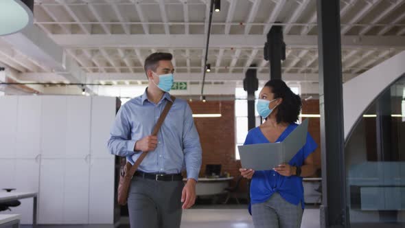 Diverse race male and female businessmen walking discussing through corridor wearing facemask