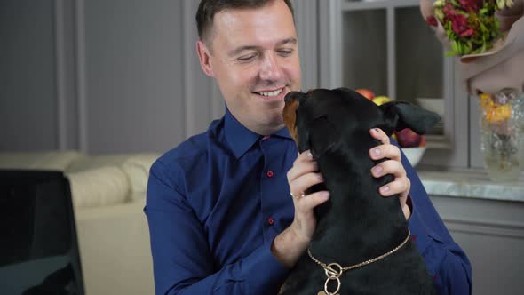 Millennial Freelancer Man is Working From Home with His Computer in Office and His Dog Distracts Him