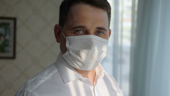 Confident business man in a medical mask at home looking to camera.