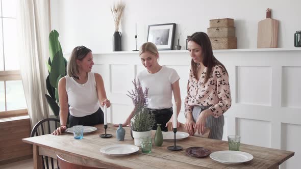 Three girls chat smile stand in the kitchen and lay out plates for a joint dinner