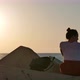 Dreaming Young Woman Sitting on the Rocks Near the Sea at Sunset - VideoHive Item for Sale