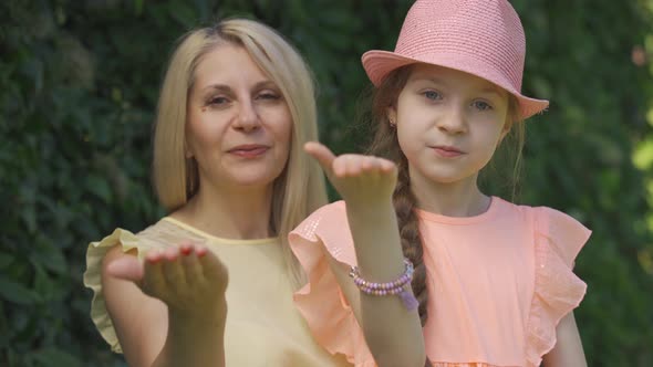 Portrait of Blond Mother and Her Little Daughter Sending Air Kiss Looking at the Camera While