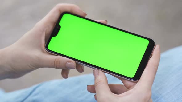 Closeup of Hands Using Smartphone with Blank Green Screen Horizontally