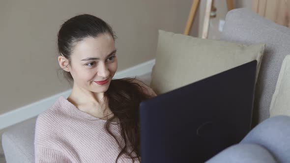 Smiling girl lying on sofa relaxing while browsing online shopping website