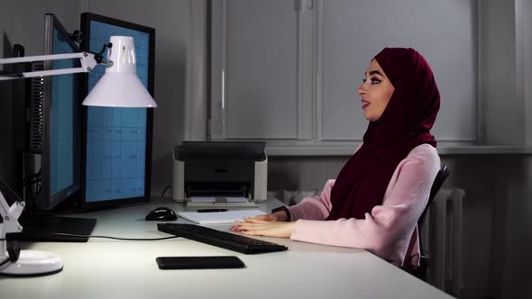 A Woman in Hijab Sits at Office in Front of Computer and Types on Keyboard