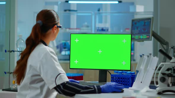 Woman Researcher Typing at Computer with Green Screen Mockup Display