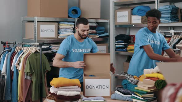 Two Male Volunteers Folding Clothes and Putting It Into the Cupboard Box at the Warehouse