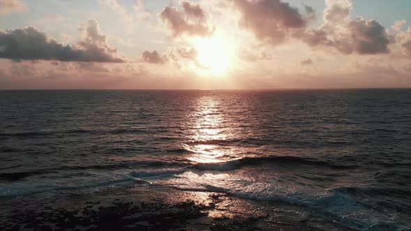 Beautiful pink sunset with sun road and gigantic ocean waves with magnificent cloudy sky at horizon