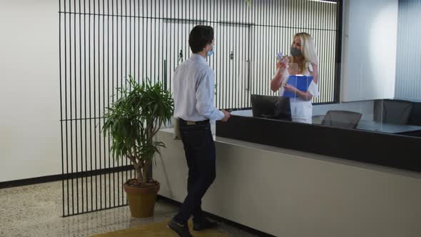 Caucasian businesswoman wearing face mask checking coworkers temperature