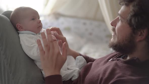 Crop father playing and talking to newborn baby at home