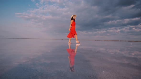 Girl in a Fluttering Dress Walks Along a Pink Salt Lake in Which the Sky Is Reflected