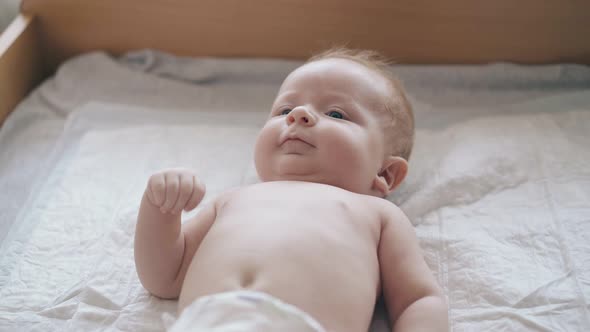 Fair Haired Infant in White Diaper Enjoys Legs Massage