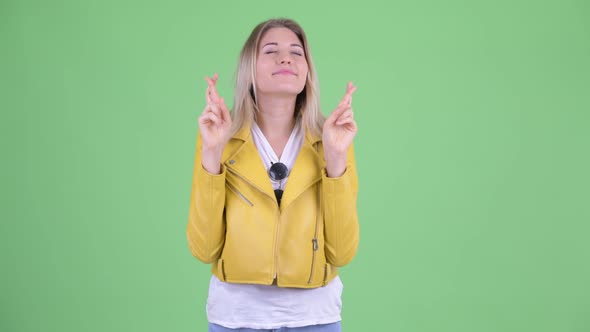 Happy Young Rebellious Blonde Woman Wishing with Fingers Crossed