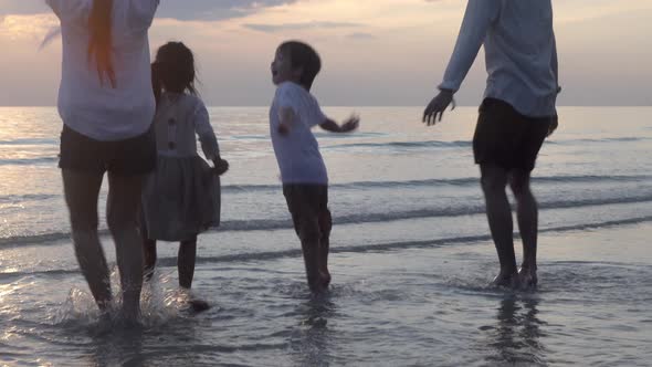 Happy asian family jump and playing water on the beach in vacation together in evening with sunset.