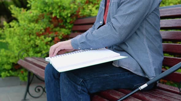 Blind Man Reading Braille Book Sitting on Bench in Summer Park