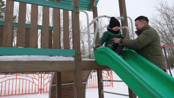 Father Helping Little Son to Slide Down the Hill