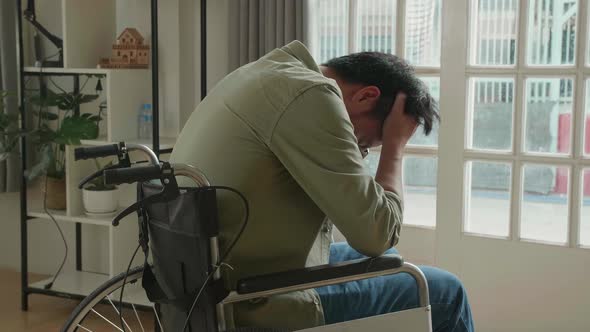 Disappointed Asian Man Sitting In A Wheelchair Near Door In The House