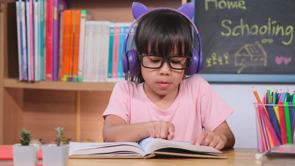 Cute little girl with headphones listening to audiobooks and looking at English learning books